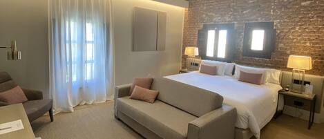 Una habitación de hotel moderna con una cama grande, un sofá, un escritorio y una pared de ladrillo.