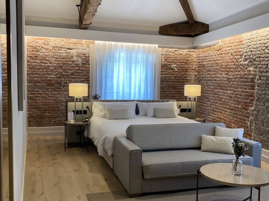 Un dormitorio con una cama grande, un sofá gris, una mesa redonda y una pared de ladrillo.