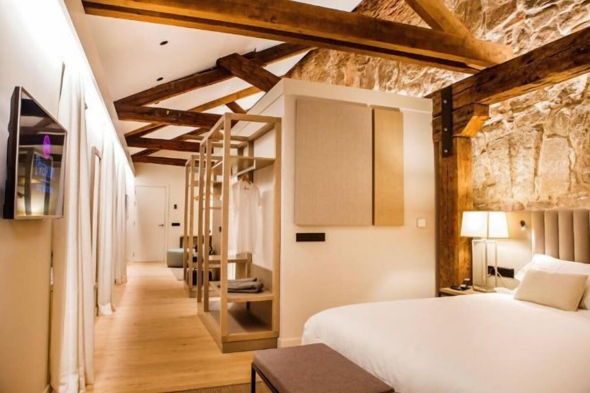 A hotel room with a wooden ceiling, a bed, a bedside table, a lamp, and a television.