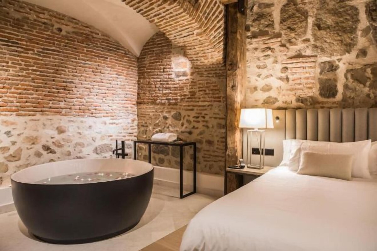 A room with a large bathtub, a bed, and stone walls.