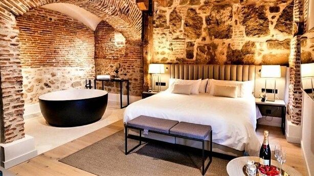 A bedroom with a large bed, a bathtub, and stone walls. - Sofraga Palacio (Ávila)