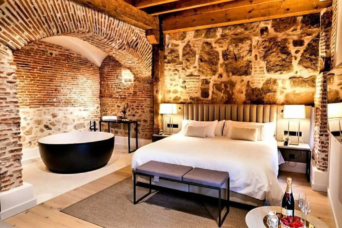 A bedroom with a large bed, a bathtub, and stone walls.