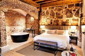 A bedroom with a large bed, a bathtub, and stone walls. - Sofraga Palacio (Ávila)