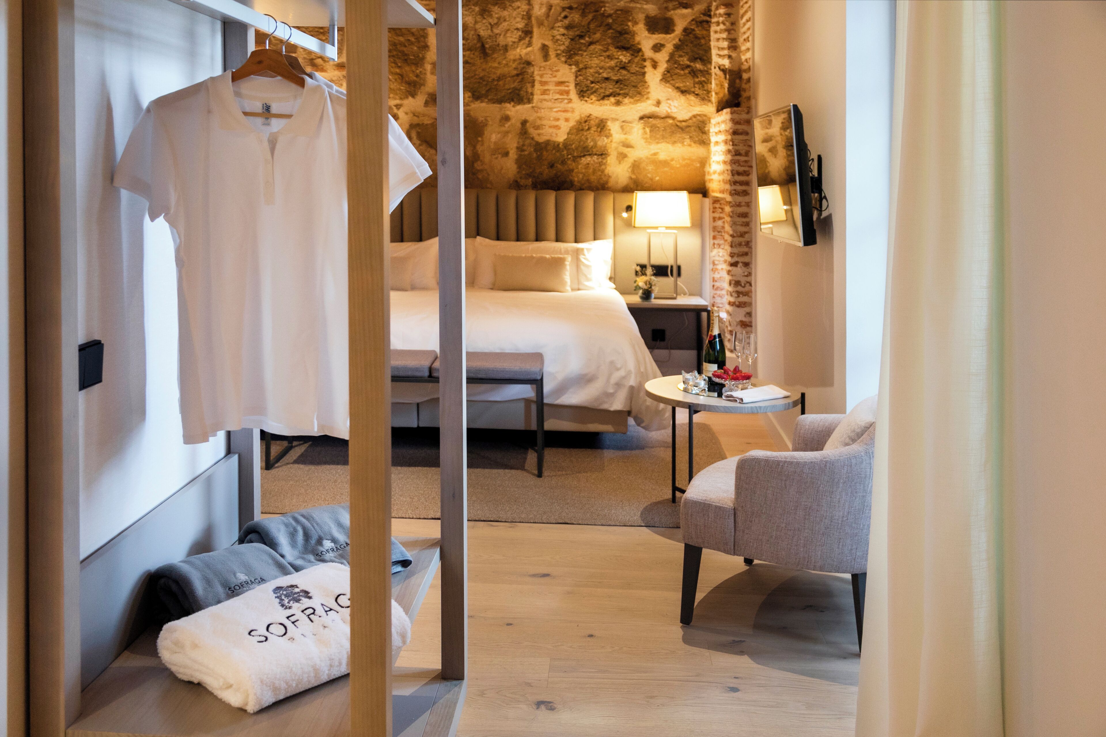 Una habitación de hotel con cama, una silla, una mesa con lámpara y una toalla colgada.
