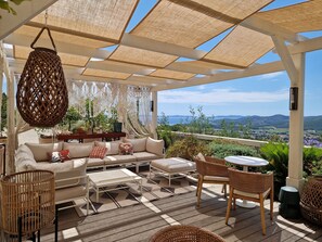 Un espacio de estar techado al aire libre con sofá, sillas y una mesa, con vistas a un paisaje pintoresco.