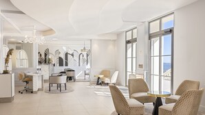 A modern hotel lobby with a round table, comfortable seating, a reception desk, and large windows offering a view. - Eden Rose Grand Hotel, BW Premier Collection (Bormes-Les-Mimosas)