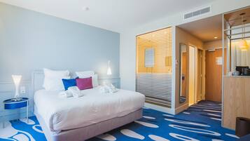 Hotellihuone, jossa on sänky, yöpöydät, puinen väliseinä ja kylpyhuoneen ovi.