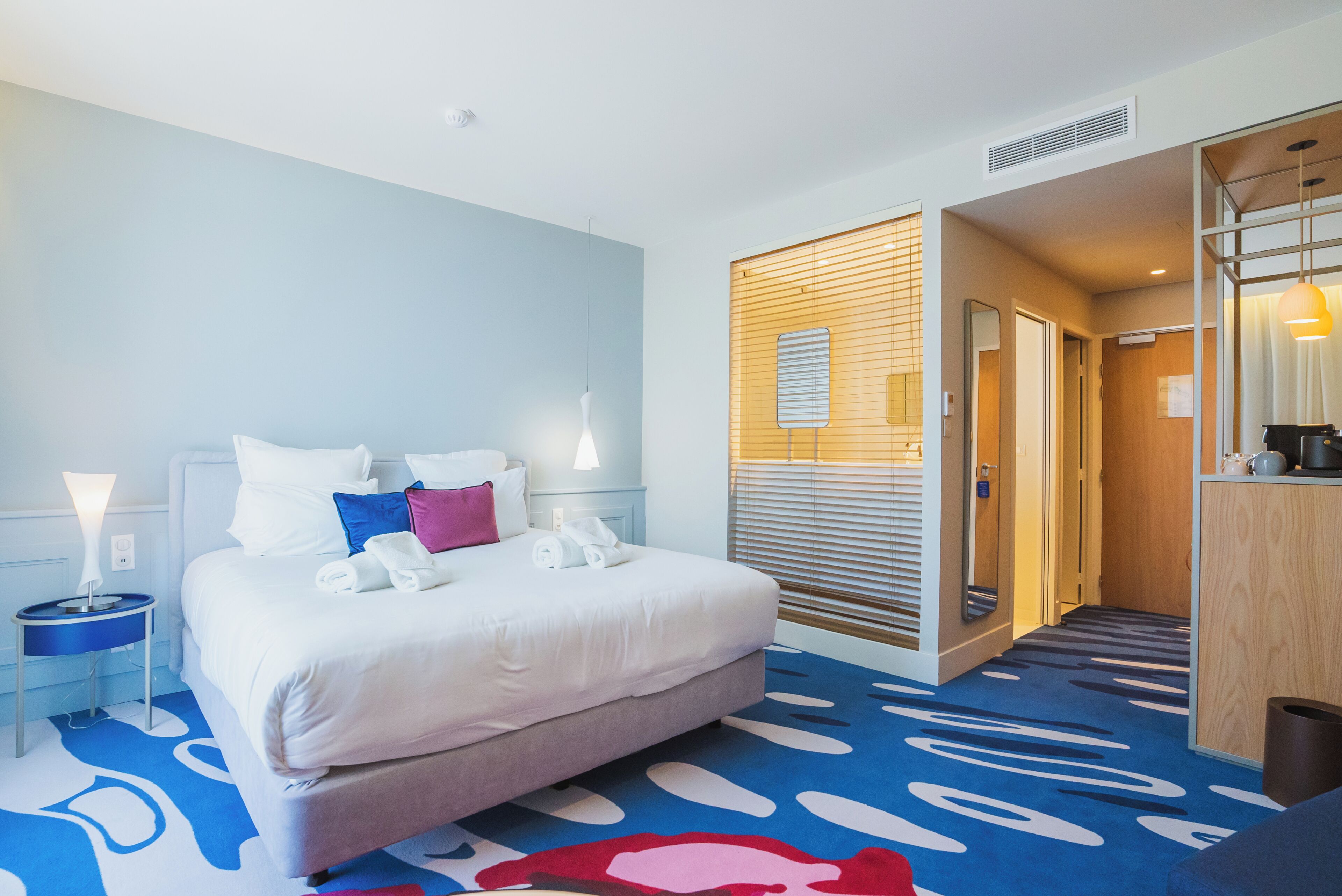 A hotel room with a bed, bedside tables, a bathroom, and a shower area.