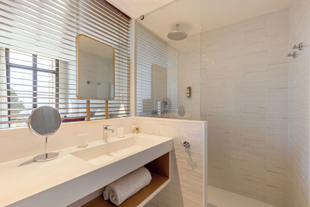 Un baño con lavamanos blanco, espejo y ducha.