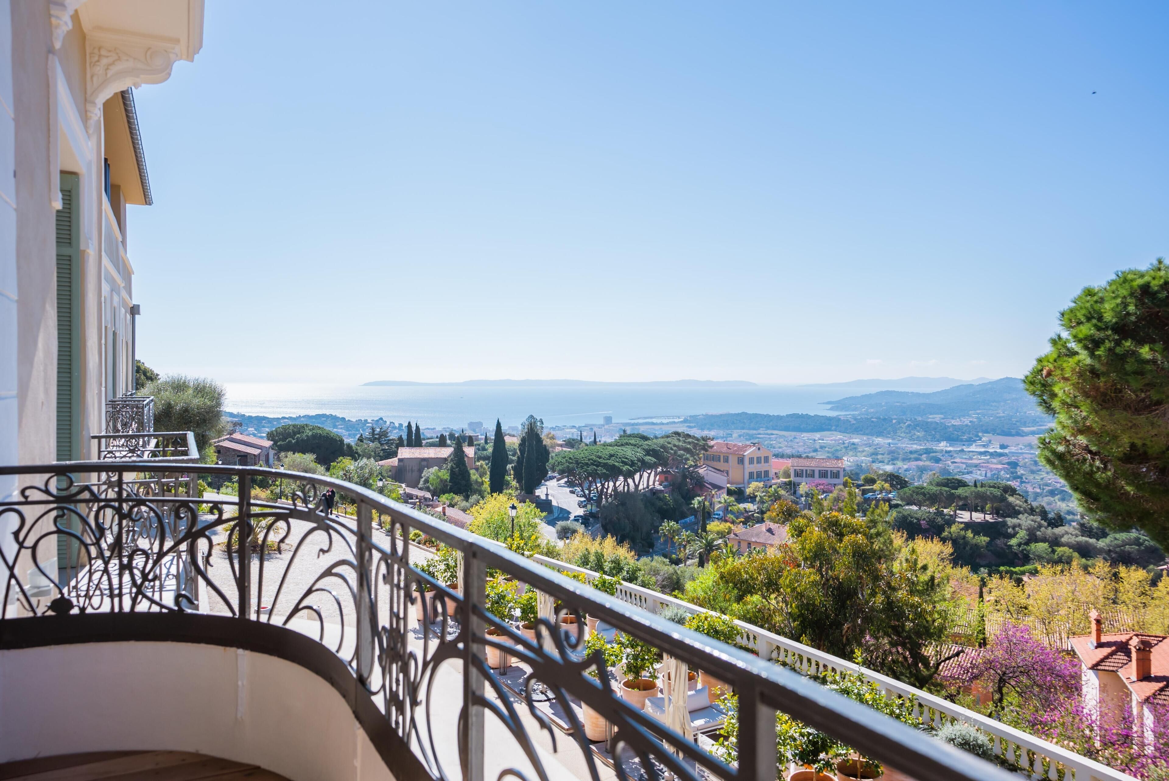 Ein Balkon mit schmiedeeisernen Geländern mit Blick auf eine malerische Stadt mit Häusern und Bäumen.