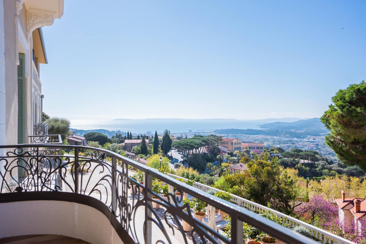 A balcony with wrought iron railings overlooking a scenic town with buildings and trees.