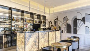 A modern bar area with a marble countertop, shelves with liquor bottles, and a seating area with round tables and chairs. - Eden Rose Grand Hotel, BW Premier Collection (Bormes-Les-Mimosas)
