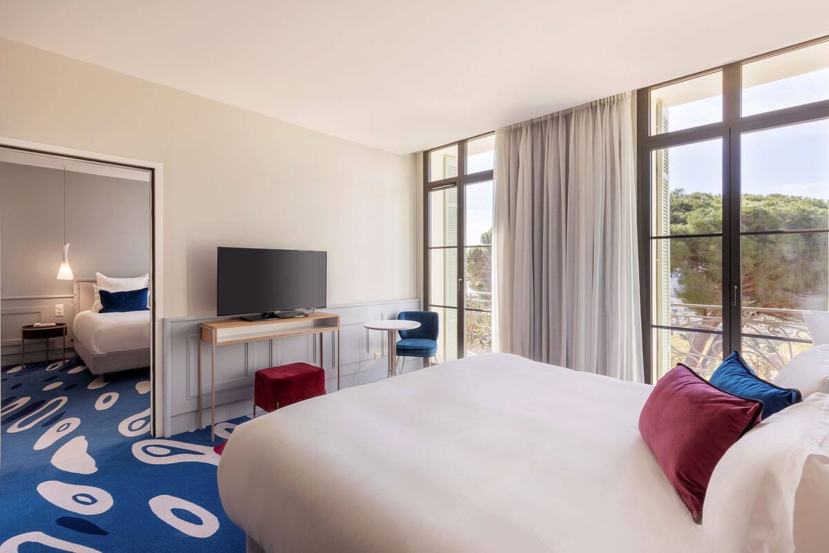 A hotel room with a large bed, a TV, a desk, a chair, and a window with a view.