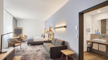 Ein modernes Hotelzimmer mit Bett, Sofa, Schreibtisch und einem Badezimmer mit Waschbecken und Spiegel.