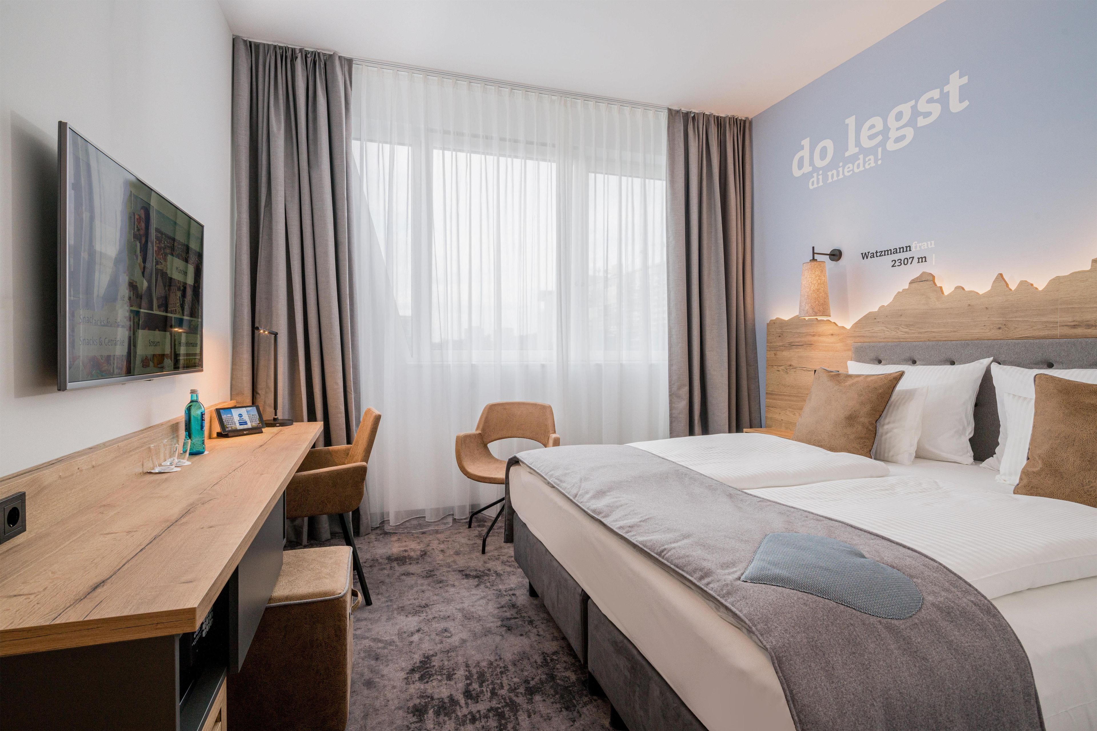 Ein Hotelzimmer mit Bett, Schreibtisch, Sessel und Fernseher.