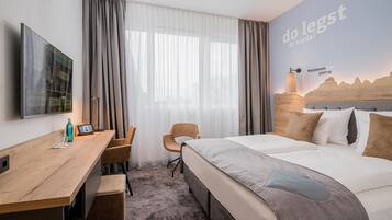 A hotel room with a bed, a desk, a chair, and a TV.