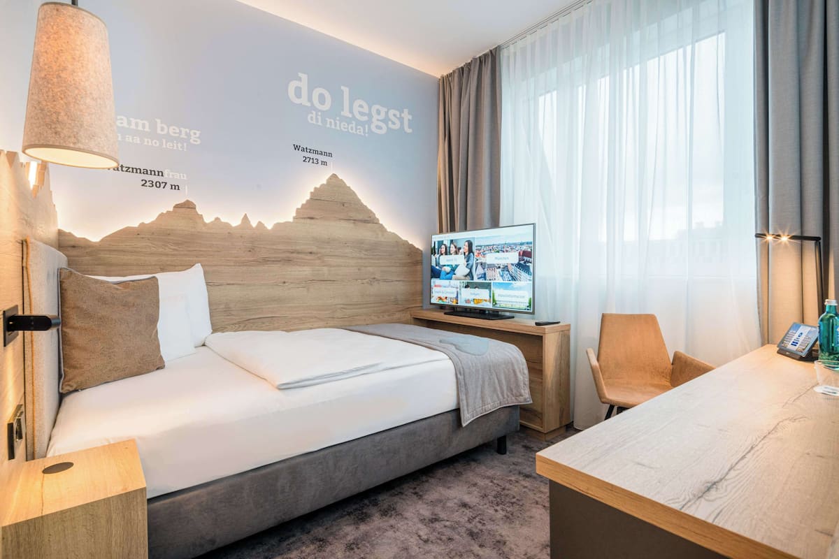Een moderne hotelkamer met een bed, een televisie, een bureau en een muur met een berg afbeelding en tekst.