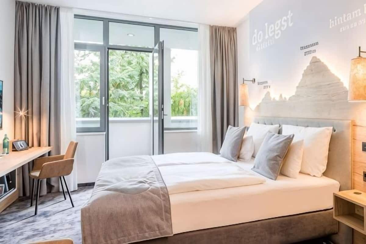 Hotelkamer met een bed, een bureau, een stoel, een raam en een muur met een bergdecor.