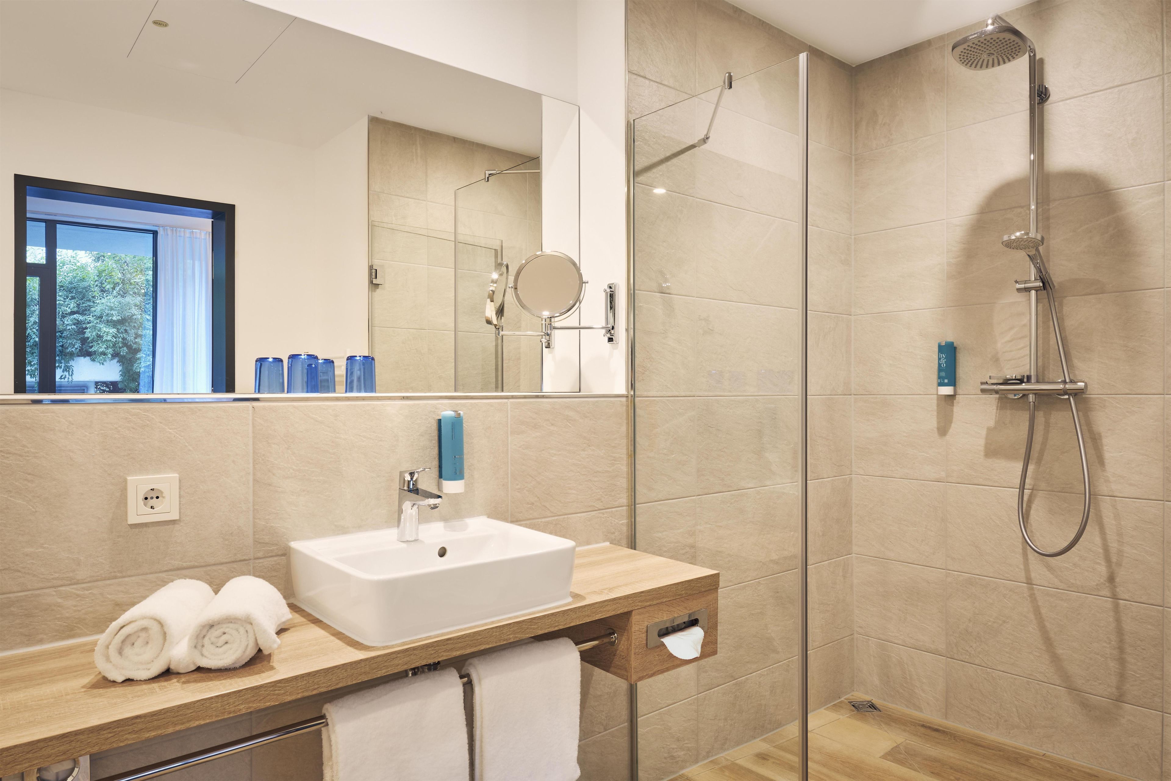 A modern bathroom with a glass shower enclosure, a sink with a mirror, and a towel rack.
