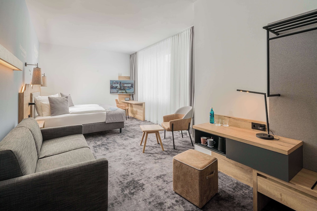 Een moderne hotelkamer met een bed, een bank, een bureau en een televisie.
