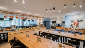 Un restaurant moderne avec de longues tables en bois, des casseroles en cuivre suspendues et une fresque représentant une vache.