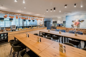 En moderne restaurant med lange træborde, hængende kobbergryder og et muralmaleri af en ko.
