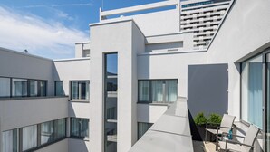 Un bâtiment moderne doté de nombreux balcons, de grandes fenêtres et d’un petit espace extérieur aménagé avec des chaises et une table.