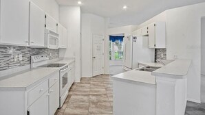 A modern kitchen with white cabinetry, a built-in microwave, and a large island with a sink.