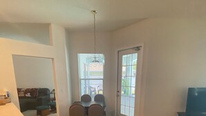 A spacious living area with a dining table and chairs, a sofa, a TV, and a kitchen area with a countertop and stools.