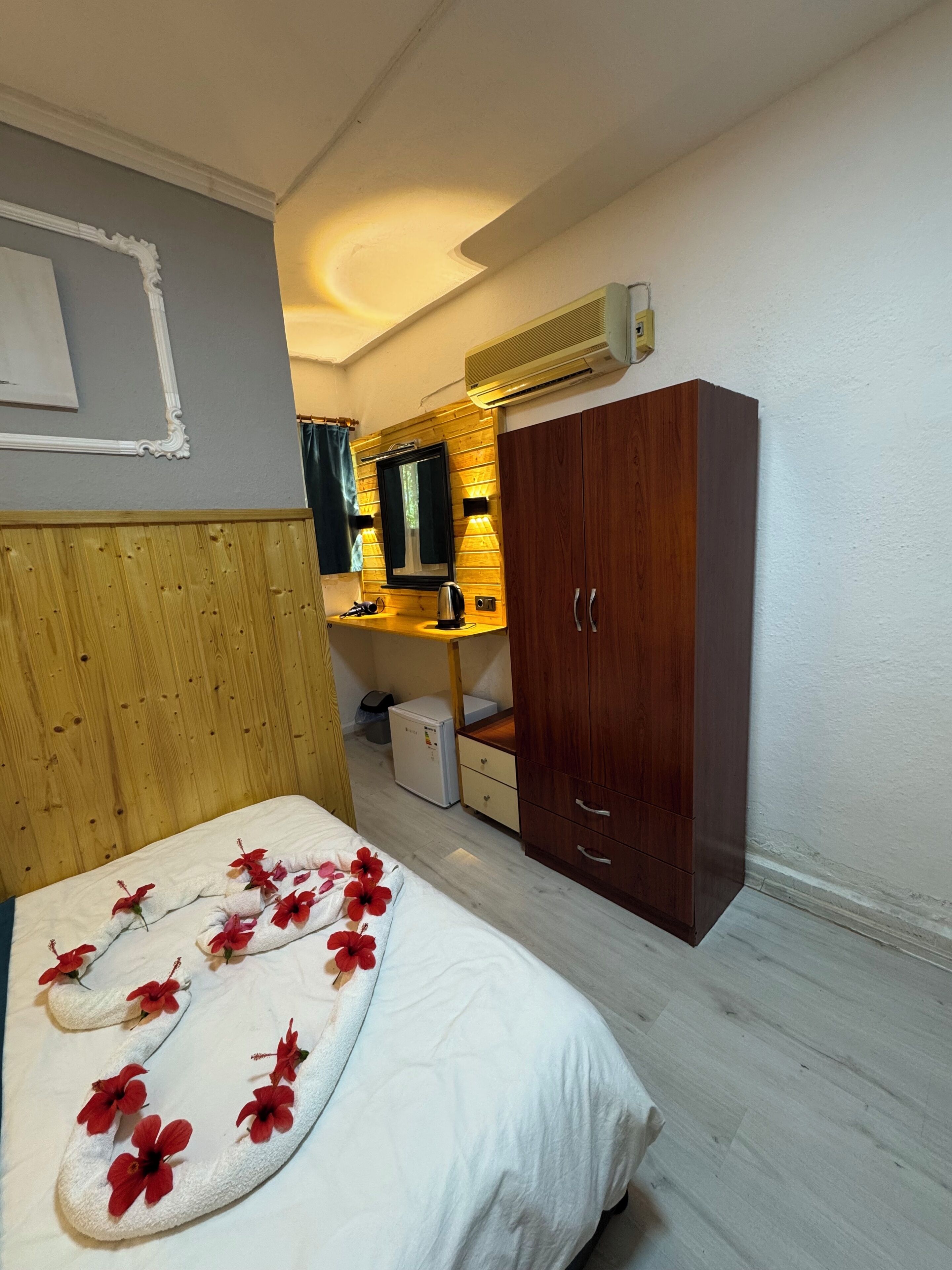 A bedroom with a bed, wooden wardrobe, a small kitchenette, and a mirror.