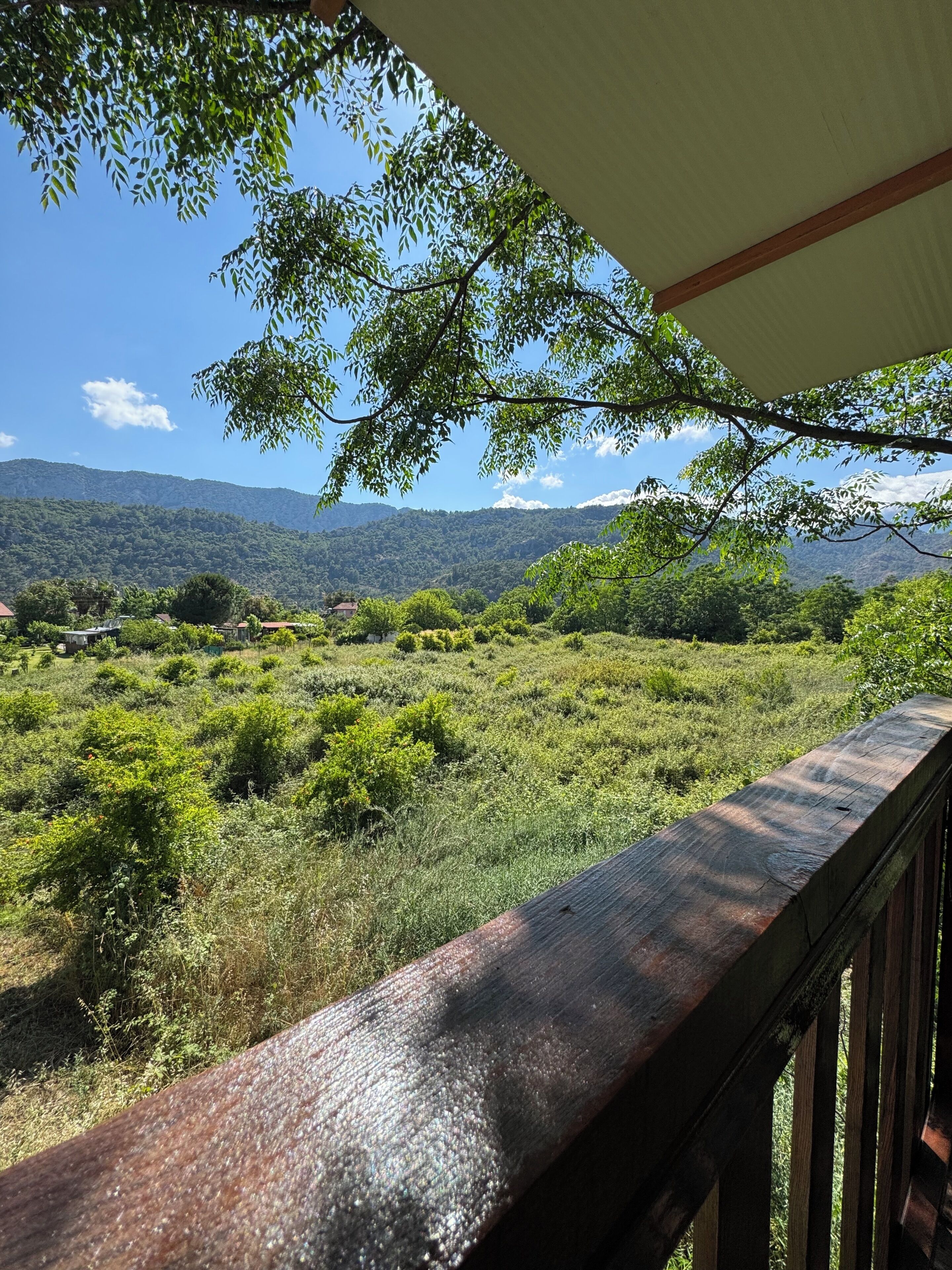 Una terraza de madera con vistas a un paisaje verde exuberante y montañas al lejano.