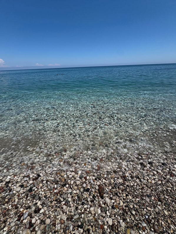 Uma praia de seixos com águas cristalinas e um horizonte distante.