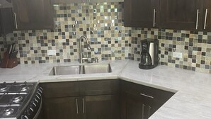 A kitchen with dark wooden cabinets, a tiled backsplash, a stainless steel sink, a gas stove, and a coffee maker. - Shedrock Shangrila, Beachfront Ocean Breeze Suite (Hopkins)