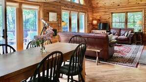 Interior acogedor de una cabaña con una mesa de comedor de madera, sillas, un sofá de cuero y un televisor.