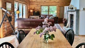 Un interior cálido de cabaña con una mesa de comedor de madera, un sofá de cuero, una chimenea y un telescopio.