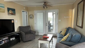 Een woonkamer met een flatscreen televisie, een grijze fauteuil, een blauwe bank en een salontafel.