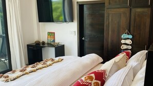 Een slaapkamer met een bed, een aan de muur bevestigde televisie, een plafondventilator en een donker houten garderobe.