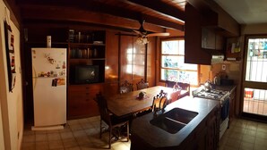 A kitchen with a wooden table, a refrigerator, a stove, and a ceiling fan. - Habitación Privada // Casa (DRN)
