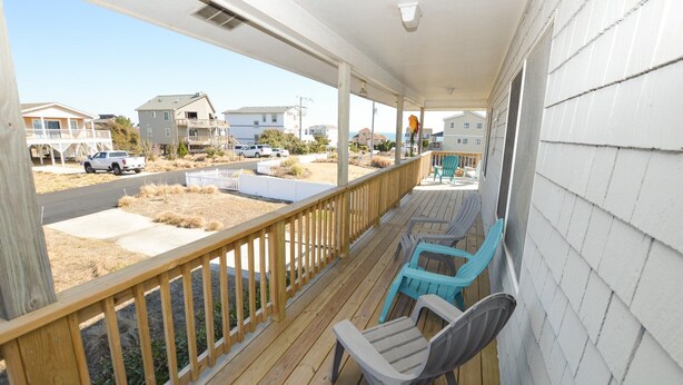 A wooden deck with a railing, two chairs, and a view of a street with houses and a truck. - This welcoming home is great for small families. (Duck)