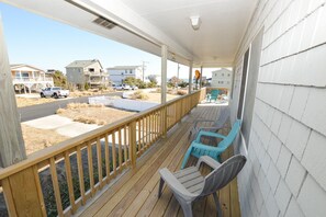 Una terraza de madera con barandilla, dos sillas y vistas a una calle con casas y un camión.