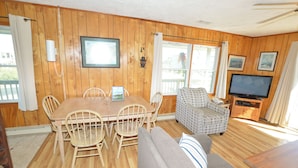 A wooden-paneled room with a dining table, chairs, a sofa, a television, and a patterned armchair. - This welcoming home is great for small families. (Duck)