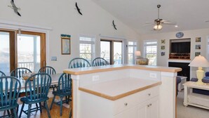 A spacious living room with a large island table, multiple chairs, and a fireplace. - Enjoy partial ocean views from this tastefully decorated home in Nags Head. (Nags Head)