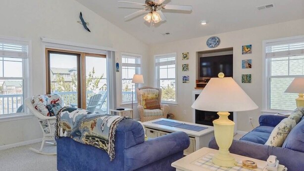 A living room with a blue sofa, a white rocking chair, a table with a lamp, and a ceiling fan. - Enjoy partial ocean views from this tastefully decorated home in Nags Head. (Nags Head)