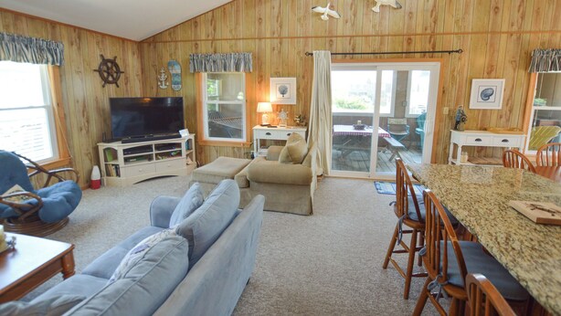 Un salon chaleureux avec un téléviseur, des sièges confortables, un coin repas avec des chaises et un intérieur en bois.