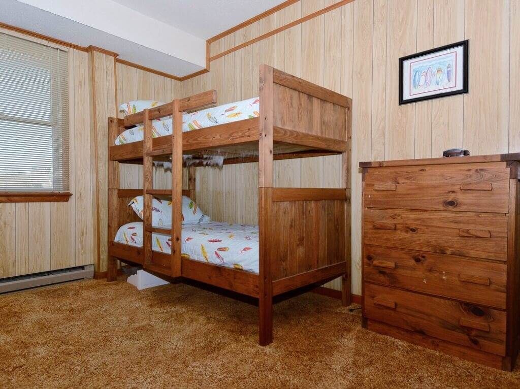 A bunk bed with a wooden headboard, a dresser with drawers, and a framed picture on the wall.