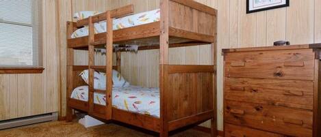 A bunk bed with a wooden headboard, a dresser with drawers, and a framed picture on the wall.