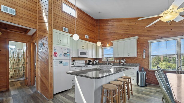 A modern kitchen with wooden walls, white cabinets, a central island with stools, and a ceiling fan.