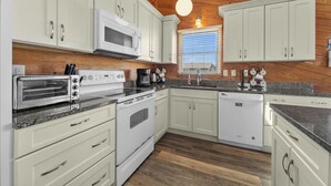 A kitchen with white cabinets, a microwave, a toaster oven, a stove, and a dishwasher.
