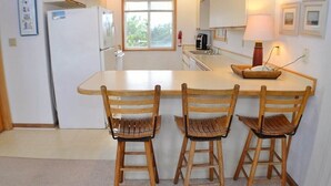 Una cocina con una isla central, tres sillas de madera, un refrigerador y un ventanal.