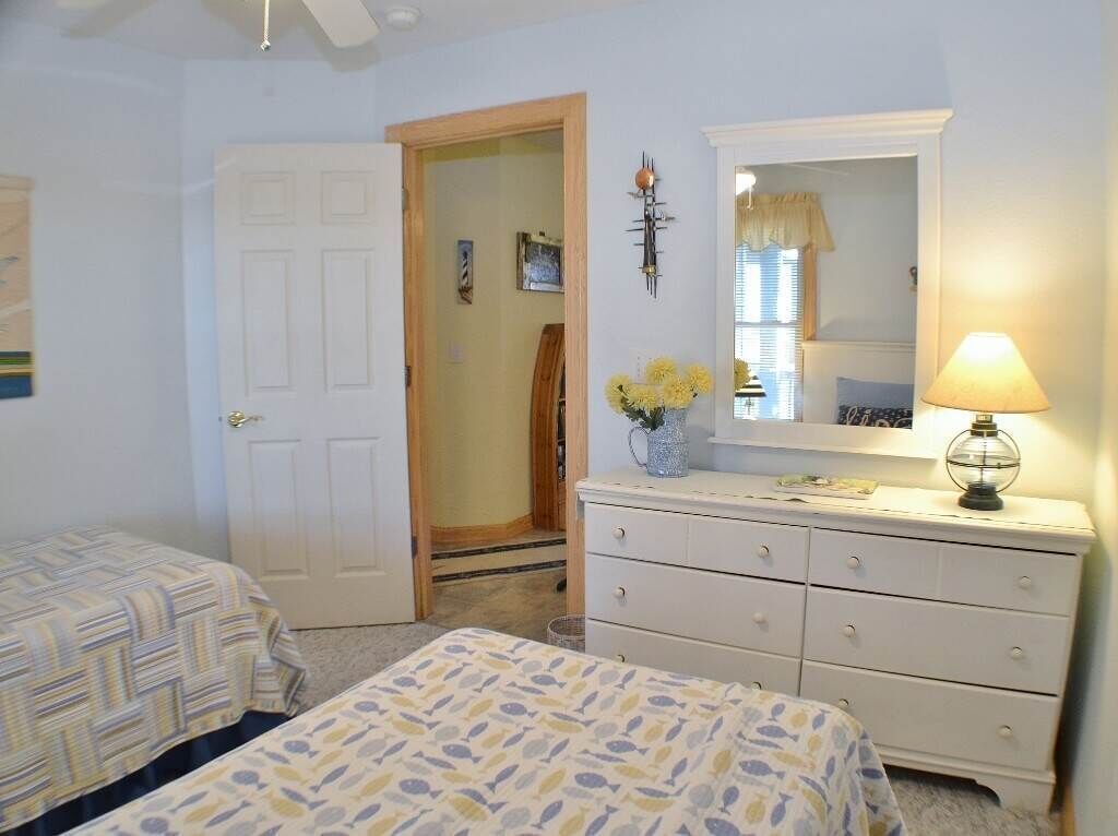 Une chambre avec deux lits, une commode, un miroir et une lampe.